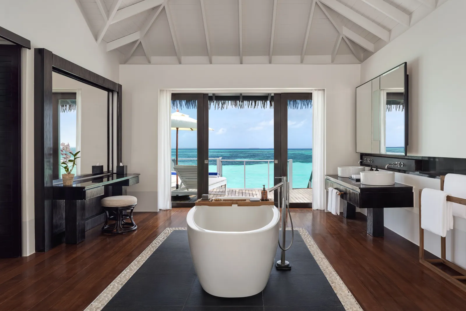 A water villa bathroom: the freestanding tub in the middle, the 2 basins, the glass doors open onto the deck and the lagoon.