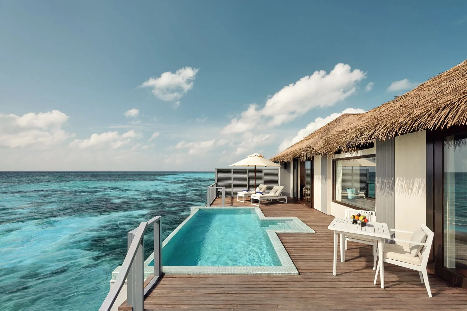 An ocean-view water villa’s deck, with its private pool, the loungers under the parasol and the open sea.