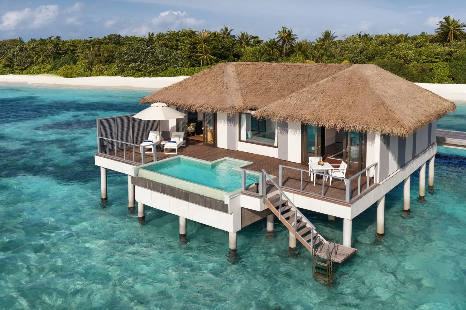 A sunset-side water villa from above: the pool on its deck, the ladder into the lagoon and the island behind.