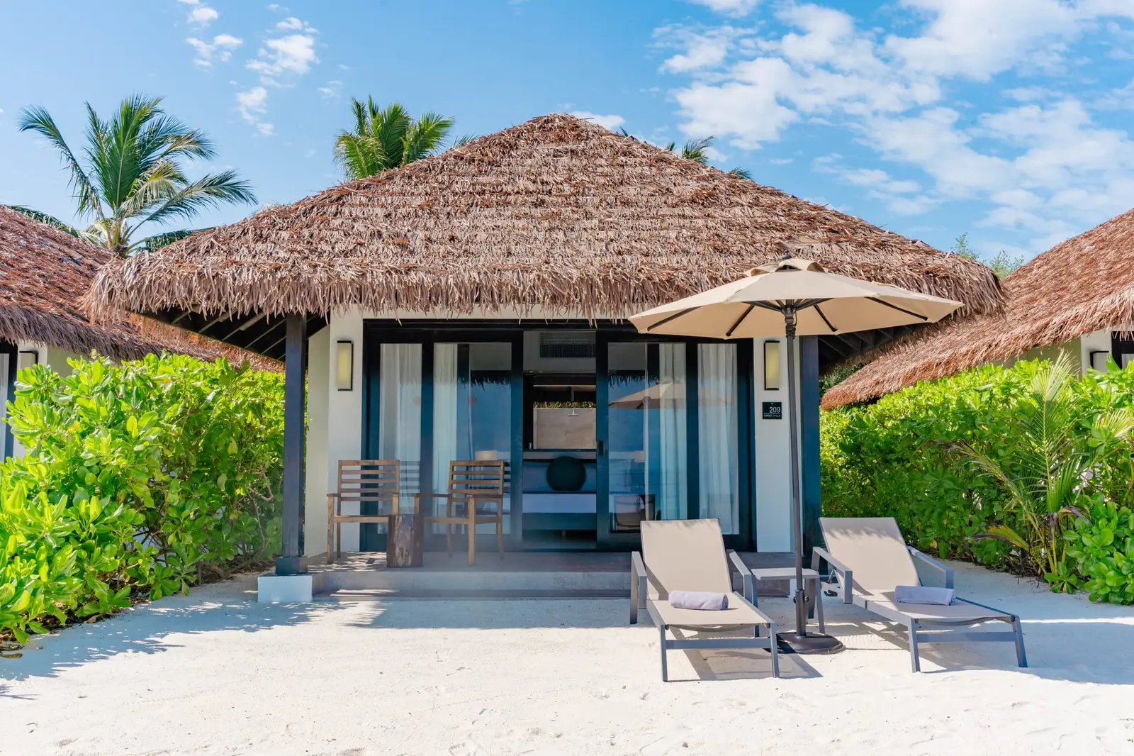Sunset Beach Villa facade on sand, with loungers and vegetation
