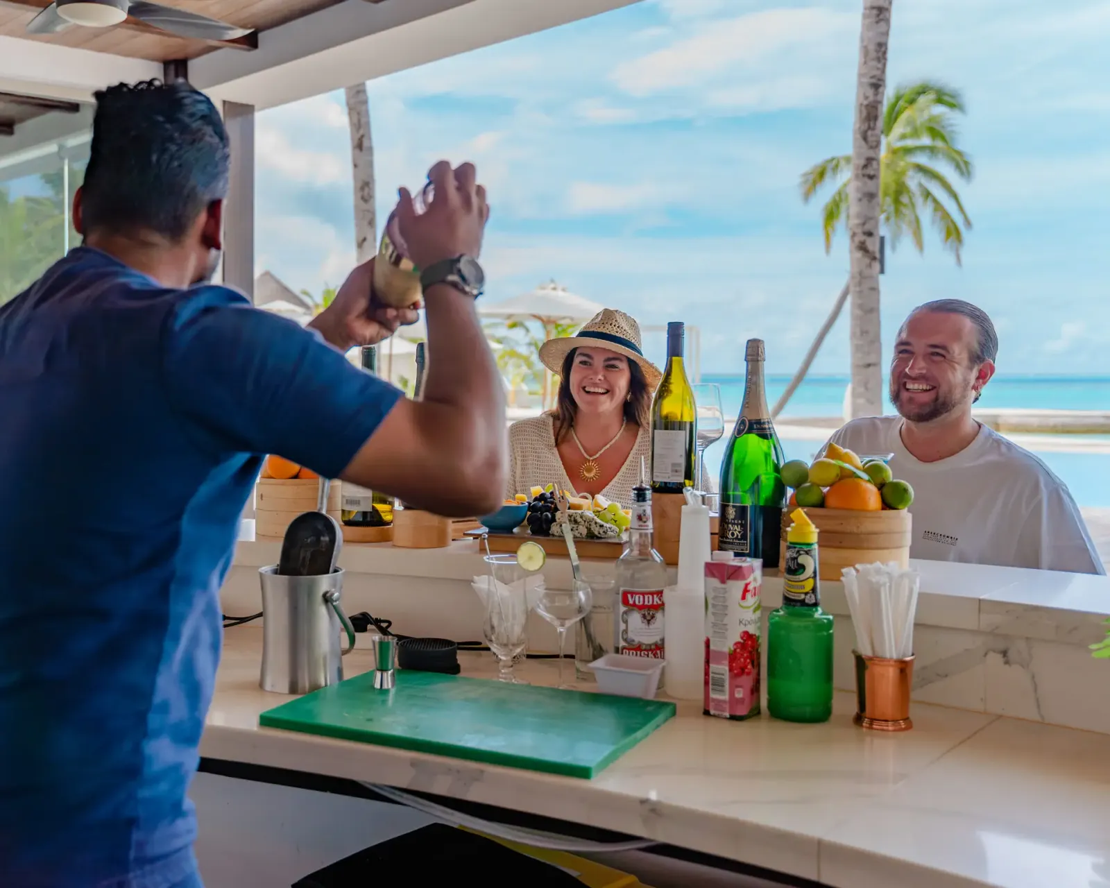 Bartender and guests at Veli bar with palms and water behind