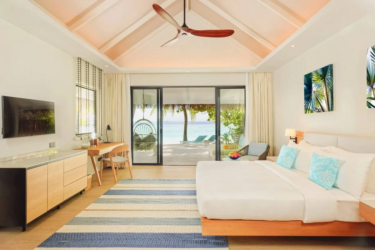 A king bedroom with a timber floor and an opening towards the beach.