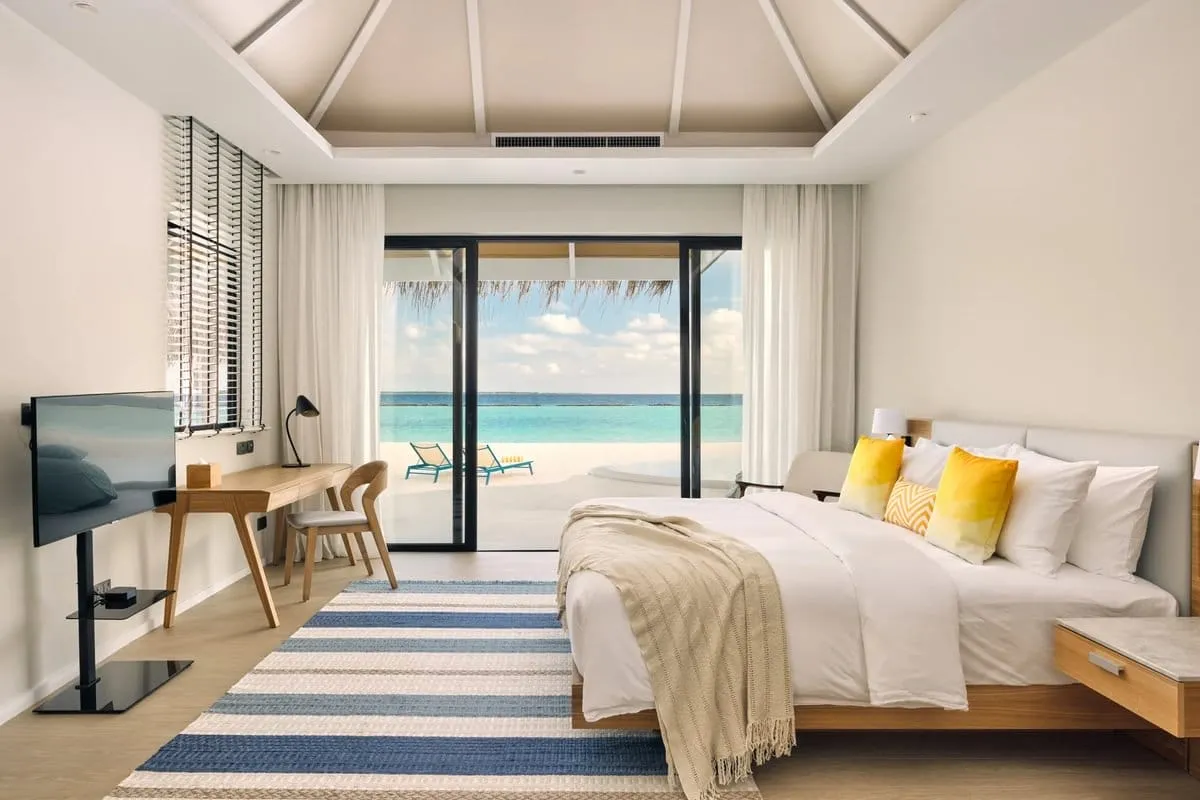 One residence bedroom, with a king bed, yellow cushions and glazed doors towards the beach.