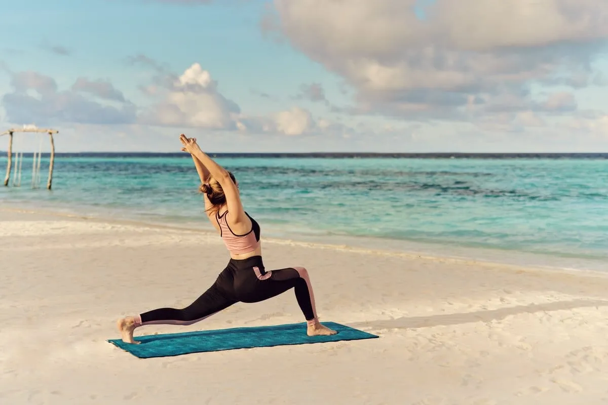 A woman stretching on the beach beside the sea.