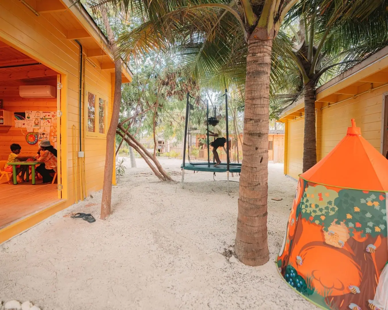Fiyoh Kid’s Club: the orange wooden huts, a trampoline under the palms and a painted tent.
