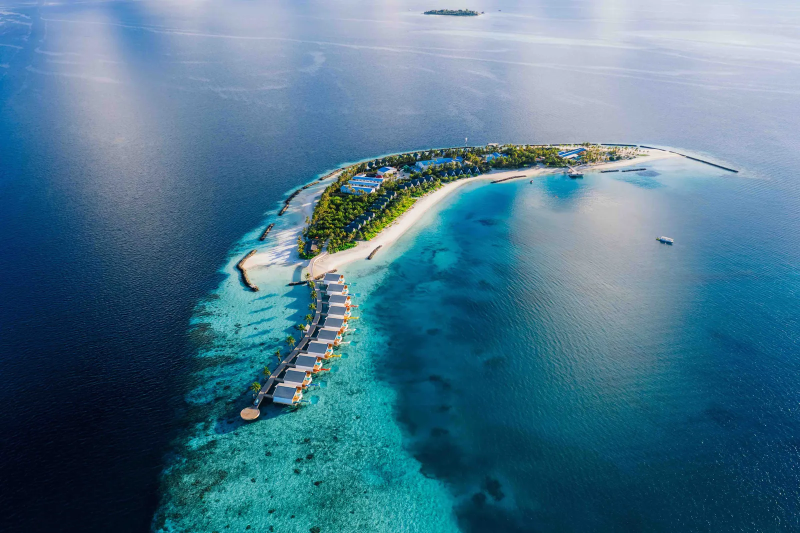Oaga from above: the long green island in its pale lagoon, with the jetty of water villas reaching out to sea.