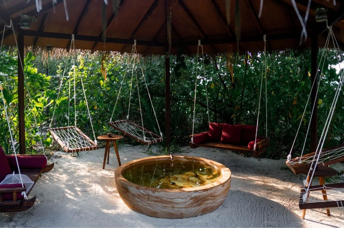 Hoba Spa’s Ufaa Lounge: rope swings and red cushions under a thatched roof, around a stone basin.