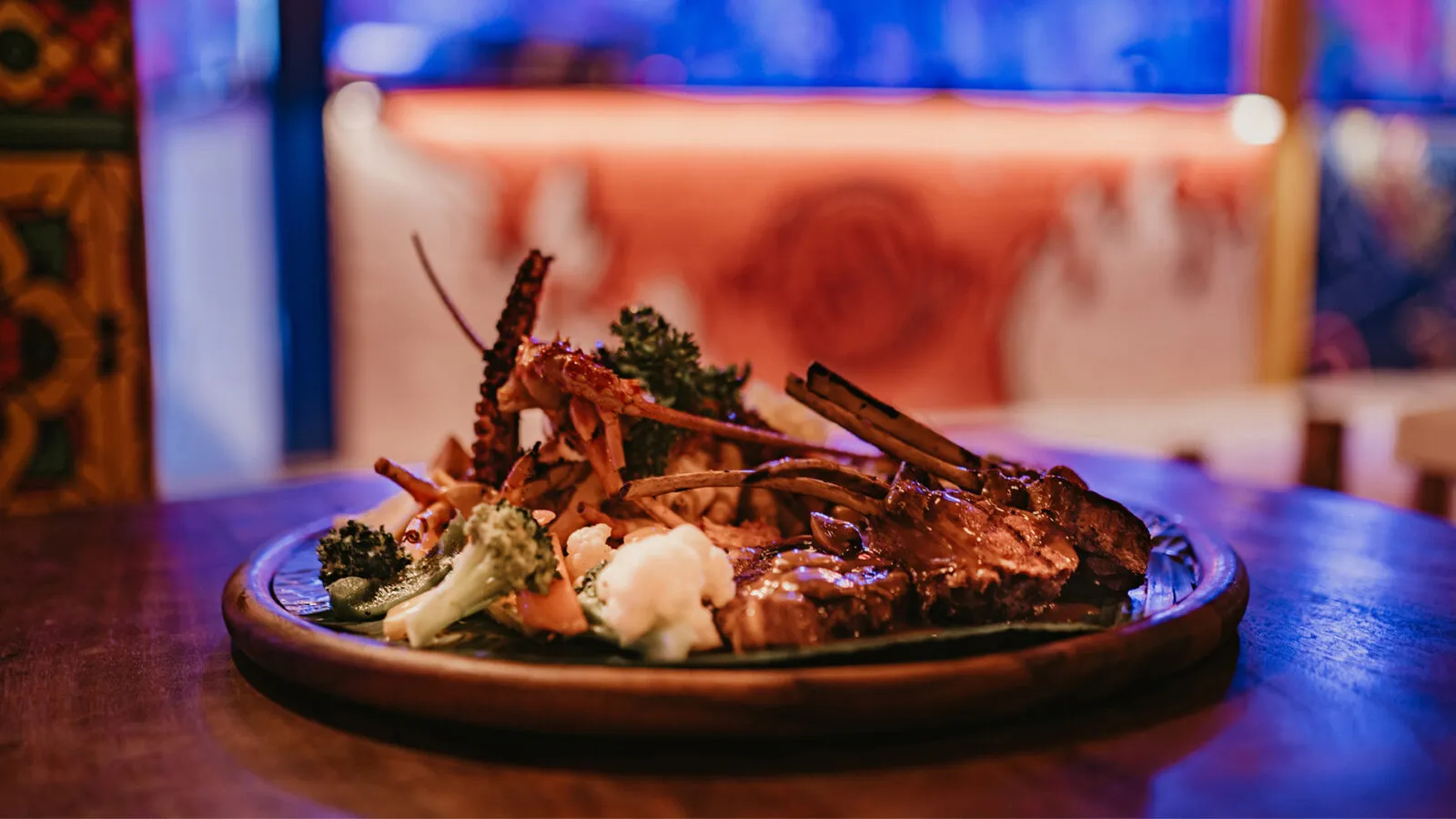 A plate of lobster and grilled meat at Kaa Kada, on a wooden table.