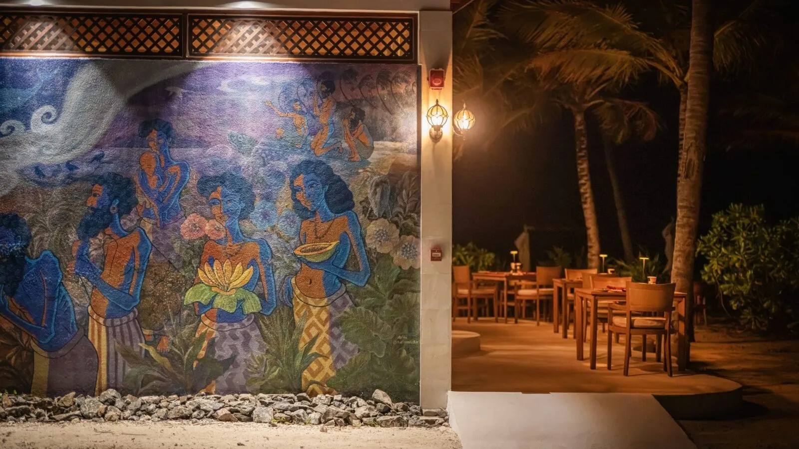 La Fuh Dan in the evening: a large mural of Maldivian figures beside the outdoor tables among the palms.