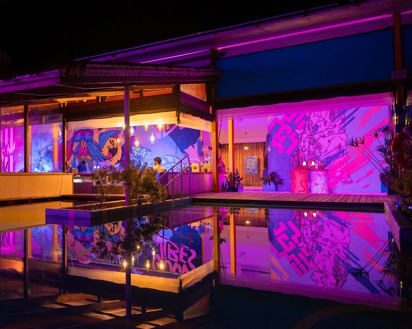 Raa Baa at night: the murals lit in violet and pink, reflected in the pool.