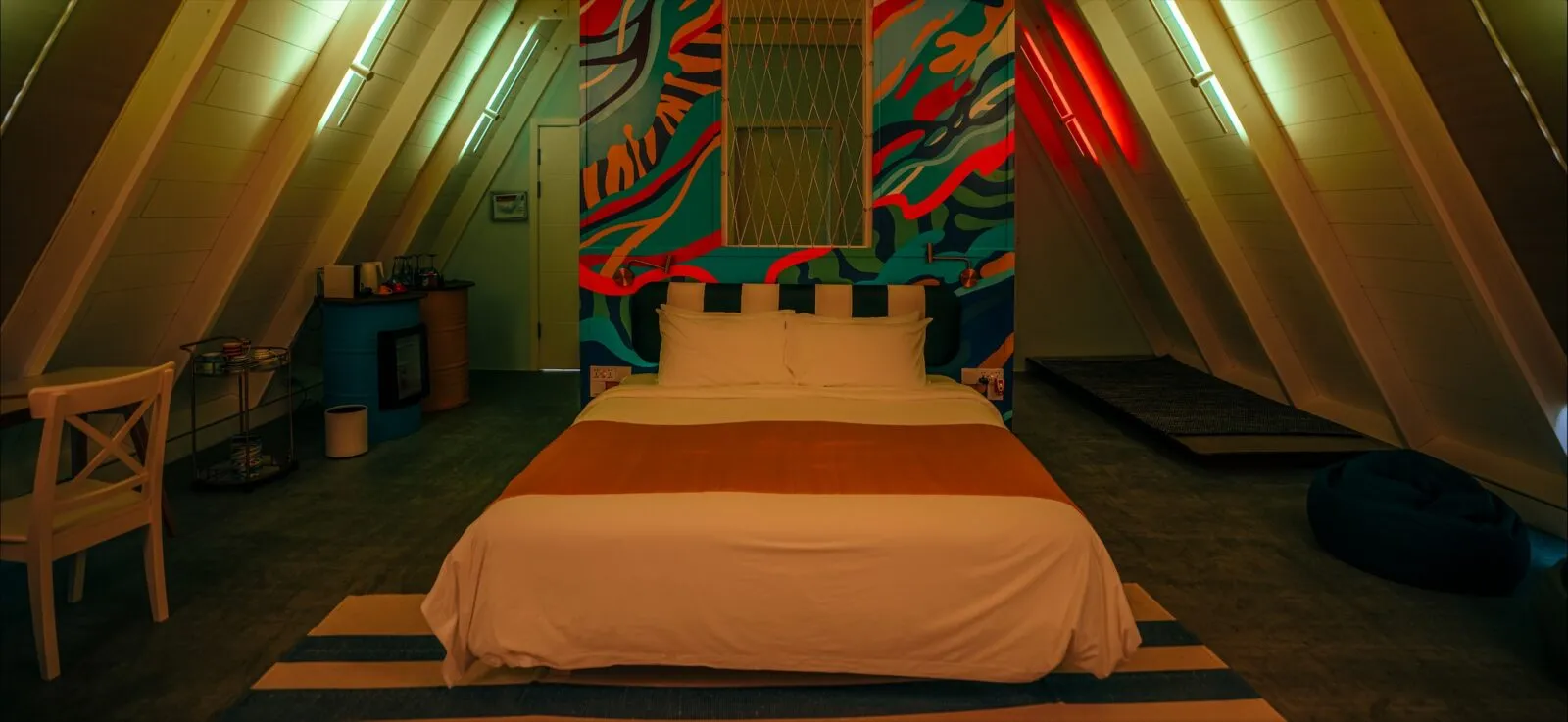 An A-frame bedroom with the bed in the middle and a colourful mural on the end wall.