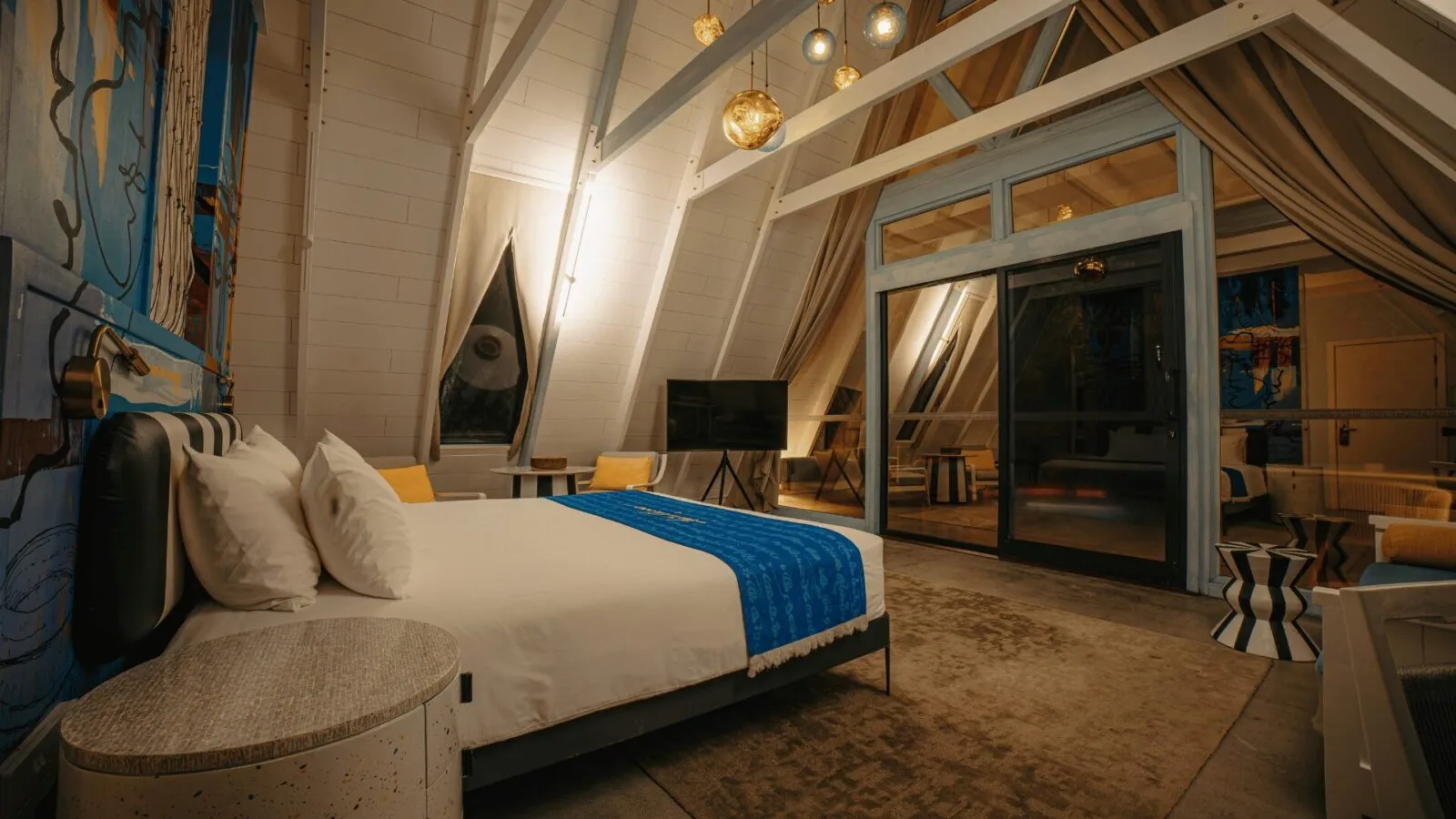 Inside a Haruge Beach Villa: the bed under the A-frame roof, the white beams and the glass wall onto the garden.