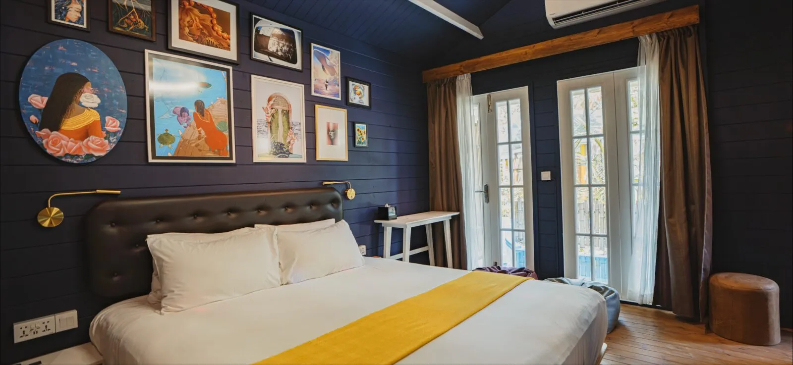 A Veyoge Gallery Pool Villa: the bed with its yellow throw beneath a wall of paintings by Maldivian artists.