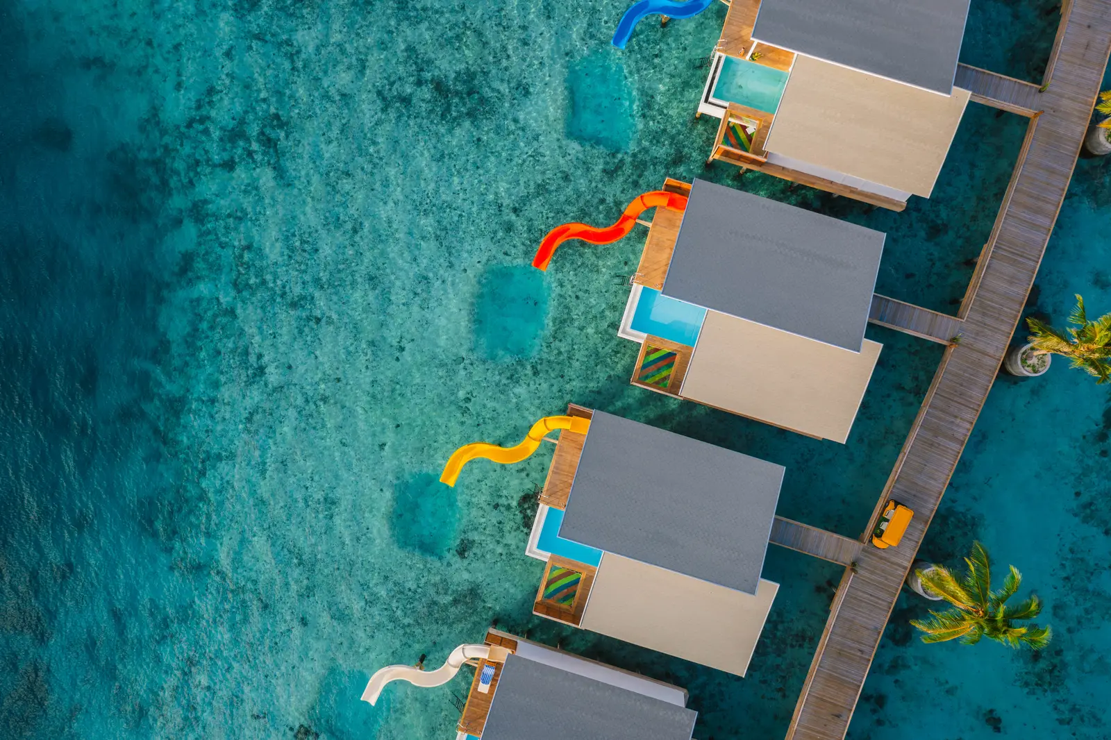 The Odi Water Villas seen straight down: grey roofs, pools and coloured slides over clear water.
