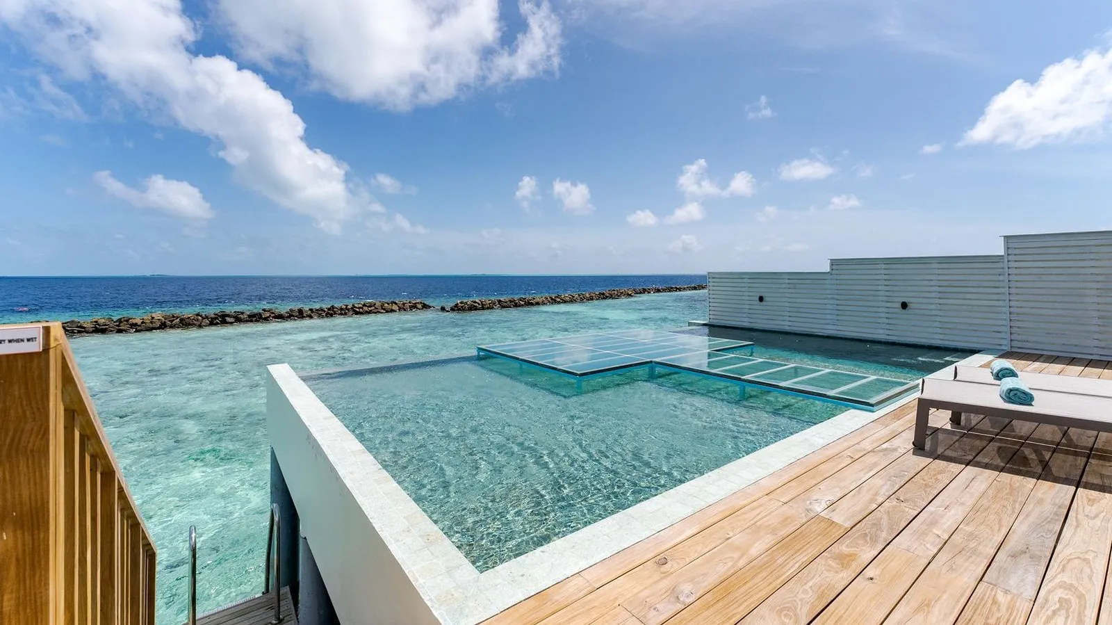 The pool of the Honeymoon Sunset Water Villa, with its glass deck panel and the ocean