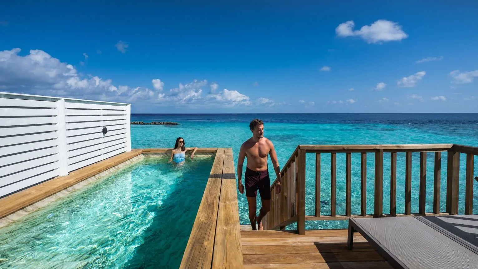 2 guests in the pool of a Sunrise Water Villa, with steps down into the lagoon