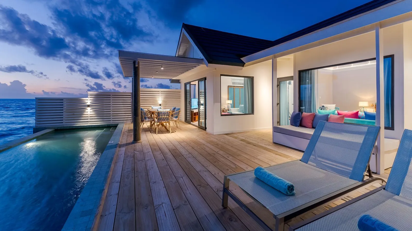 The deck of a Sunset Water Villa at dusk, with the lounger, the pool and the villa lit up