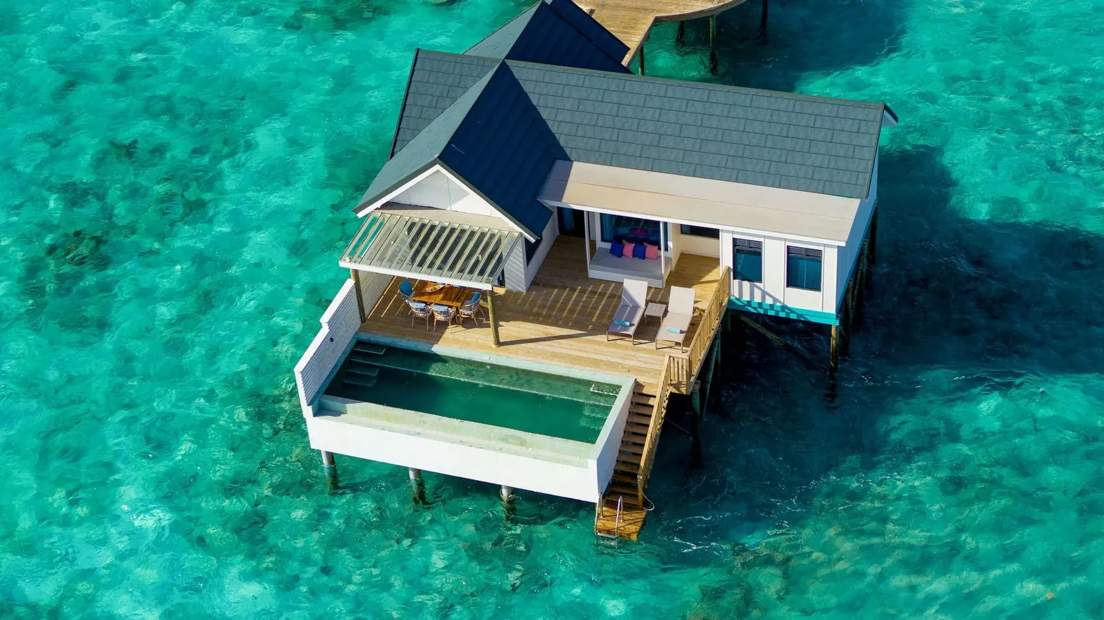 The Sunset Water Suite from above, with its blue roof, deck and pool over the lagoon
