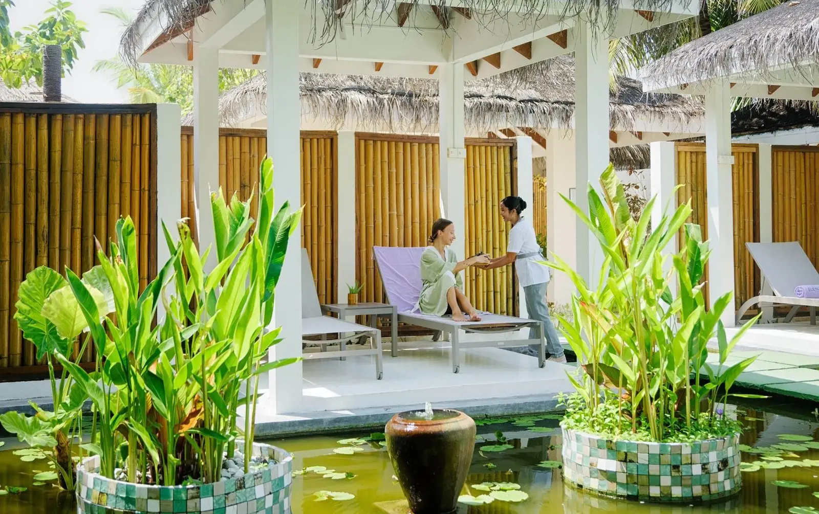ELE|NA Ayur spa: a guest on a lounger under the white pavilion, among plants and a lily pond