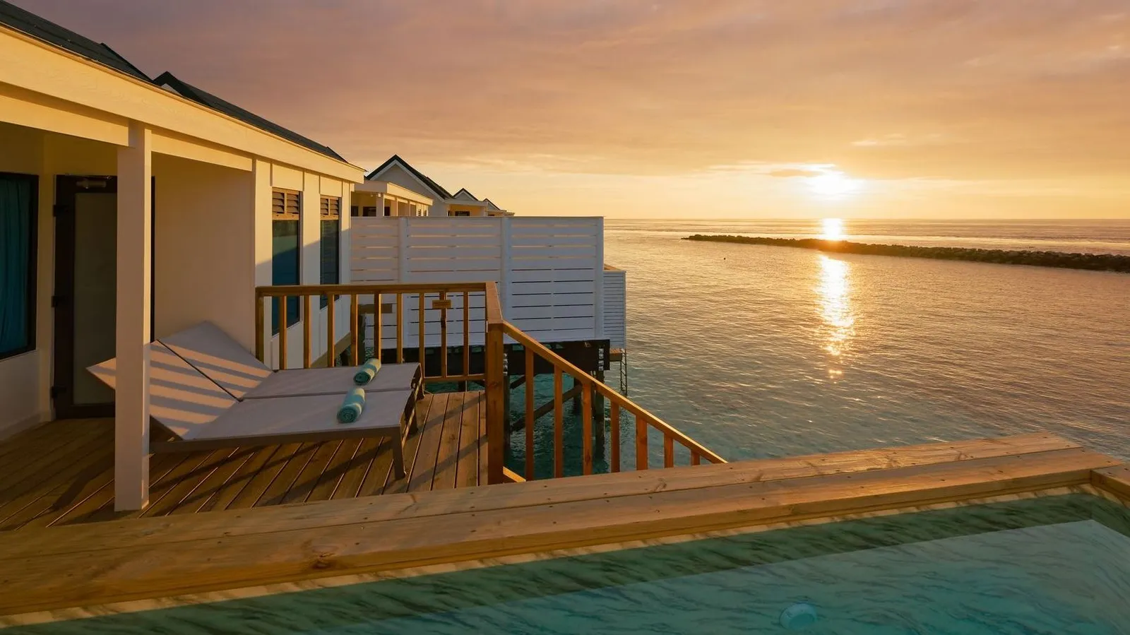 The deck of a Sunset Water Villa at sunset, with its lounger and pool over the lagoon