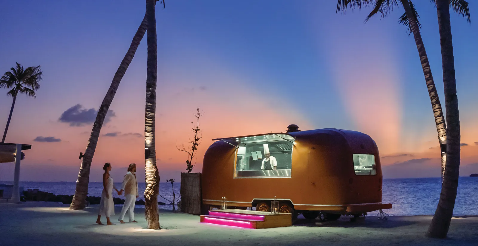 The Gaadiya 17 food truck on the beach at dusk, among the palms, with a couple walking up.