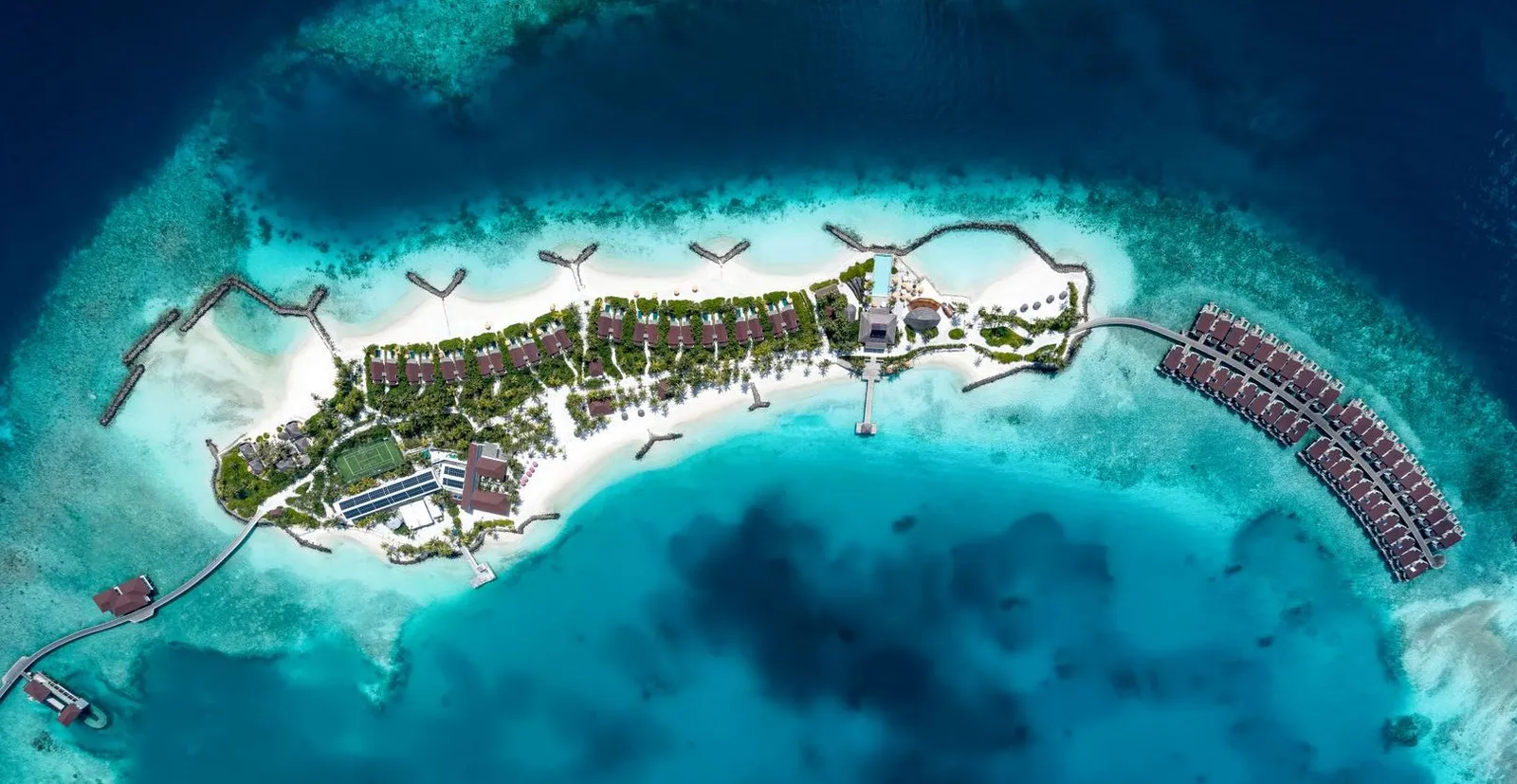The island seen from overhead, long and narrow inside the reef, with the row of water villas curving off to the right.