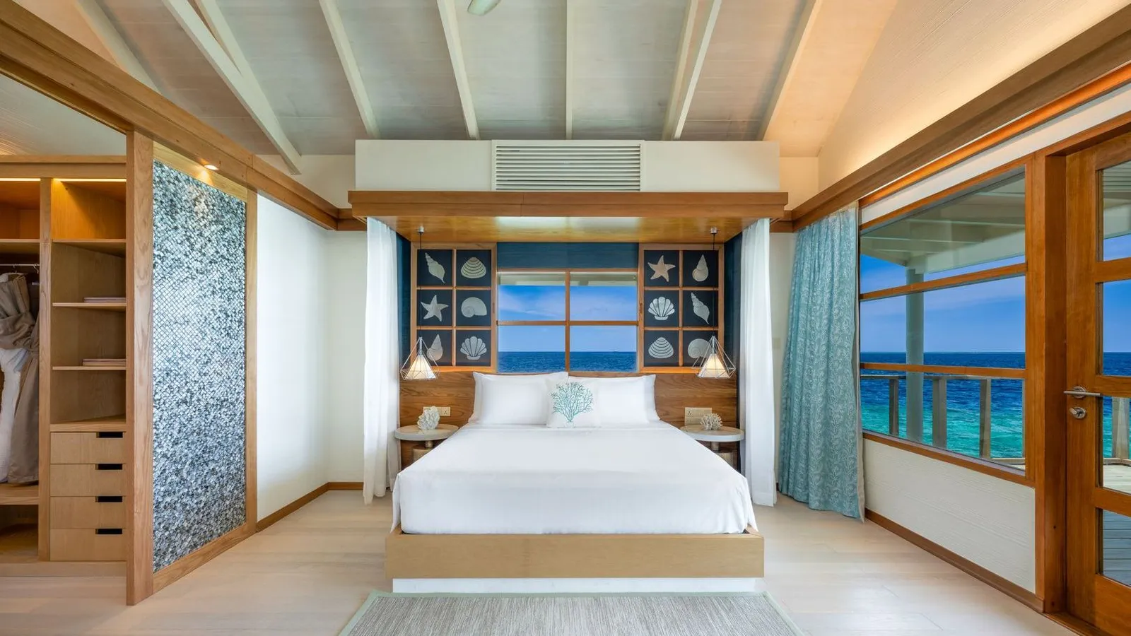 A Nest Water Villa bedroom: the king bed, the pale floor and windows onto the lagoon.