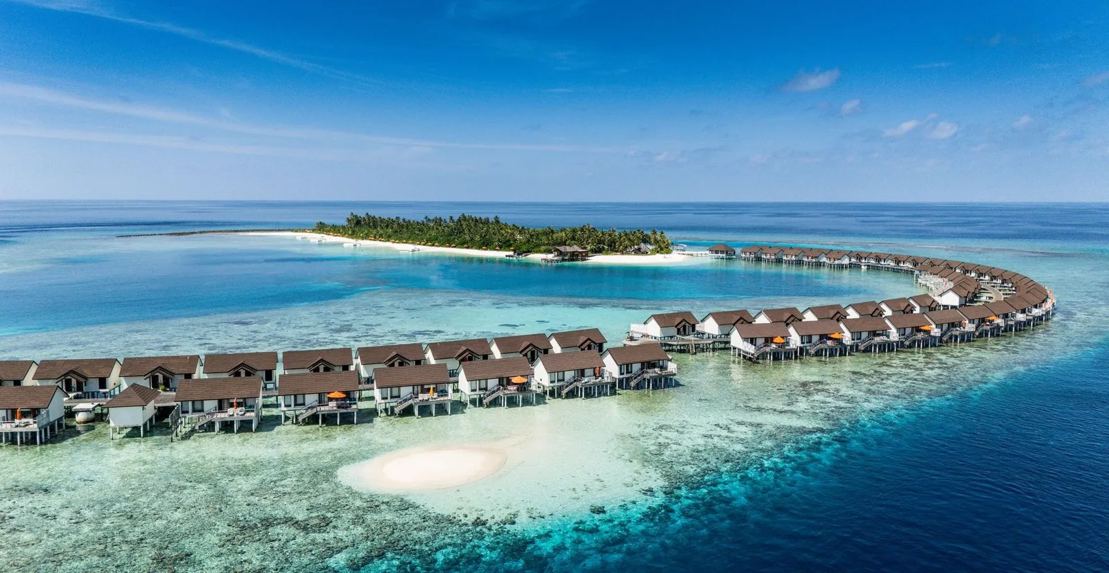 The long curve of water villas closing off the lagoon, with the green island behind.