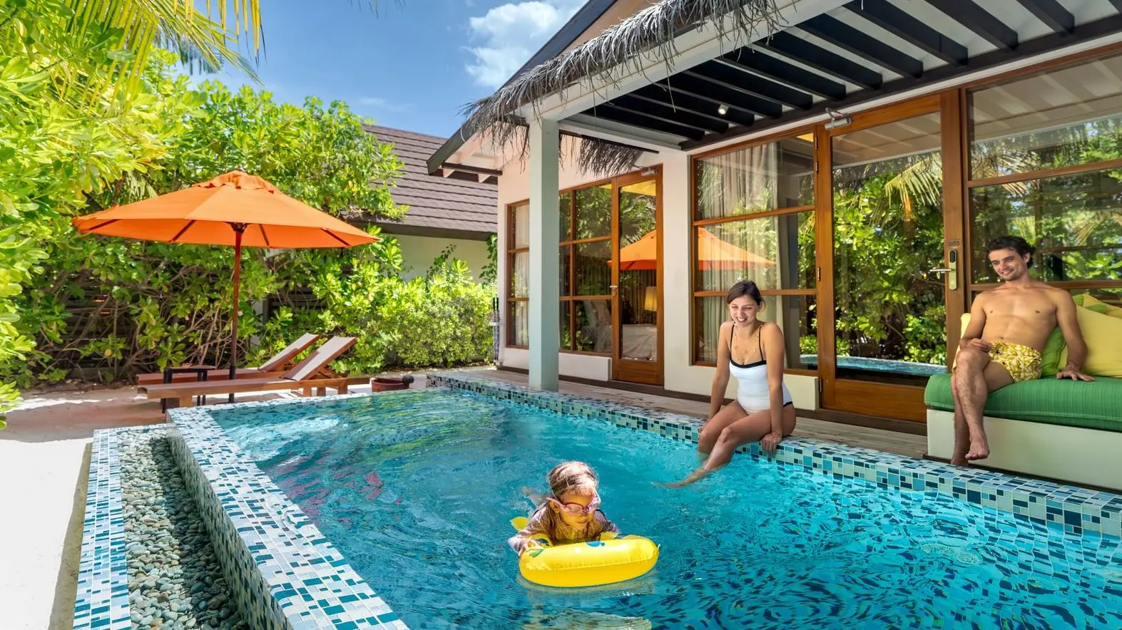 A family in a 2 Bedroom Beach Pool Suite’s pool, the little girl in a rubber ring in front of the glass doors.