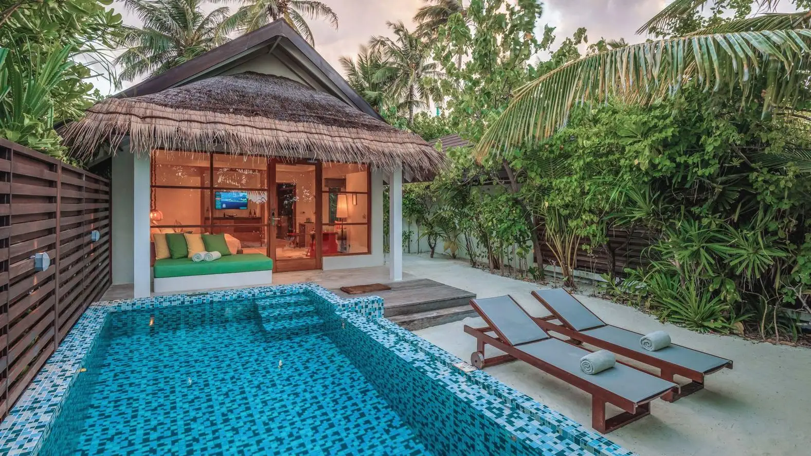 A Beach Villa with Pool: the rectangular pool in front of the villa and 2 loungers in the shade of the palms.