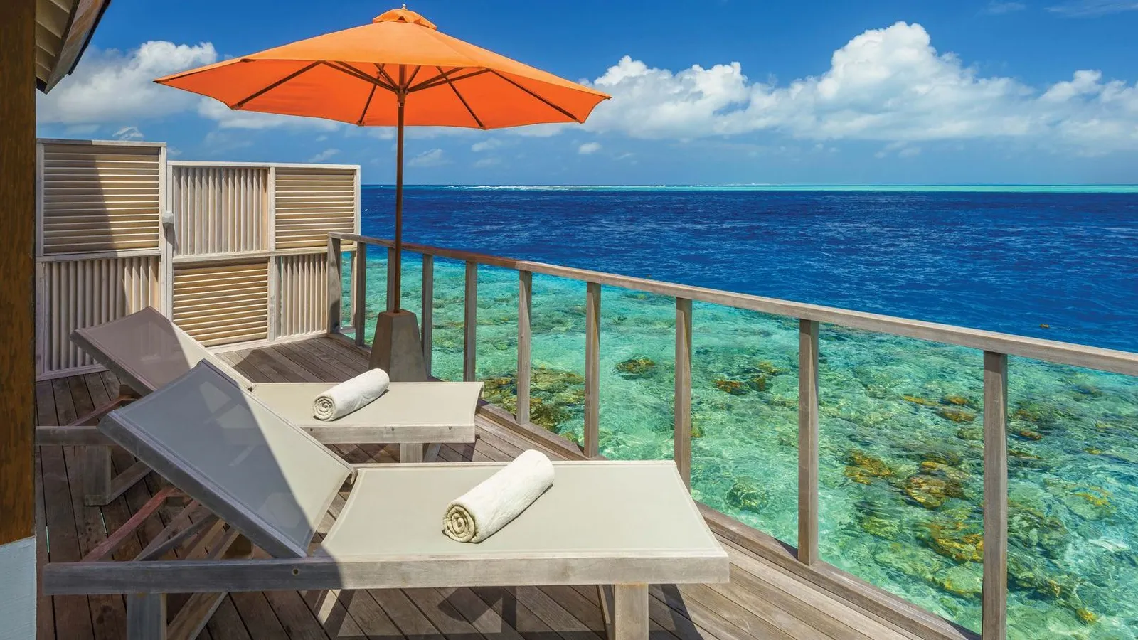 A Water Villa’s deck with the orange parasol, the loungers and the lagoon below the rail.