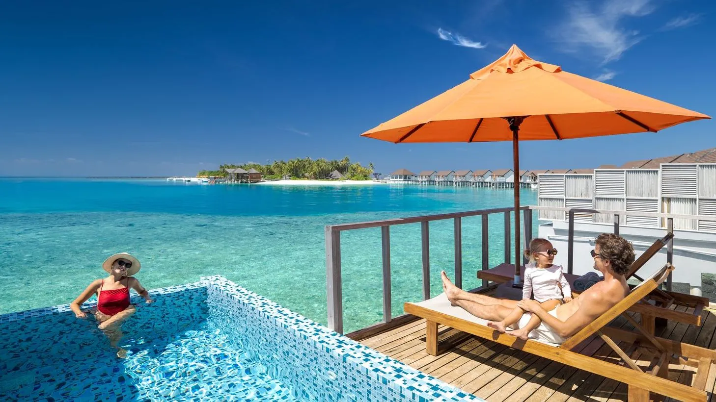 A Water Villa with Pool’s infinity pool, with a girl in the water and her parents on the lounger above the lagoon.