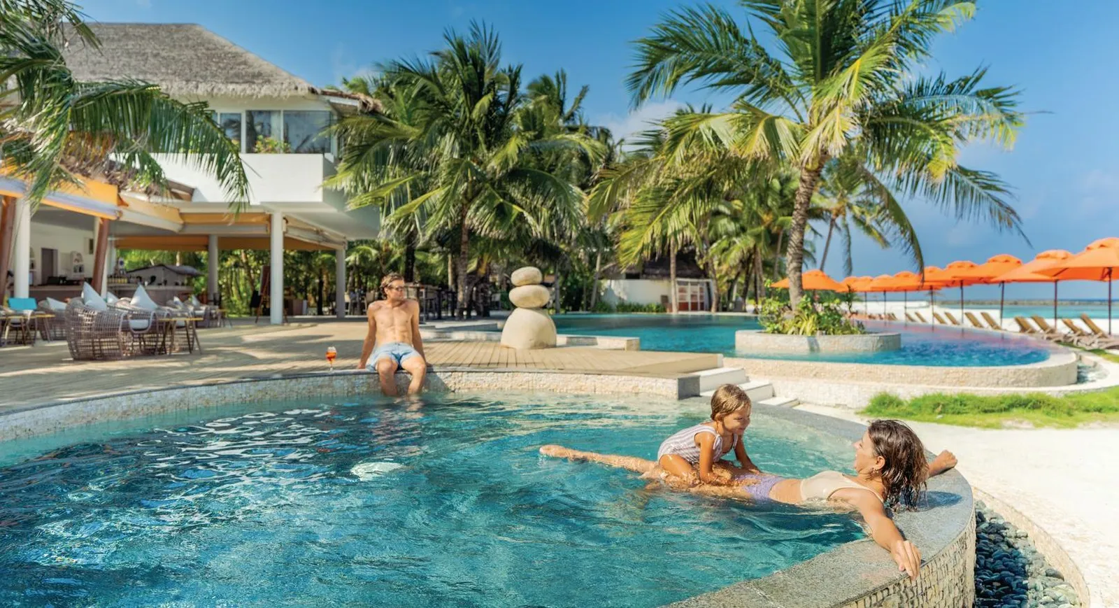 The main pool beside The Sangs, with a family in the water and palms all around.