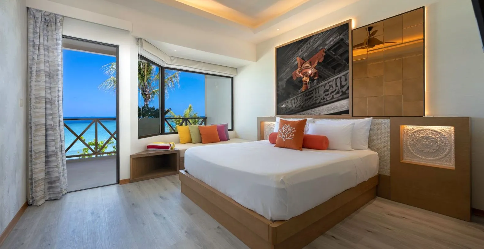An Ocean View Room: the king bed, the window seat with bright cushions and the door to the balcony.