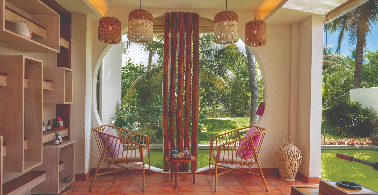 A room at ELE|NA Ayur: 2 armchairs under wicker lanterns, facing a round opening on to the garden.
