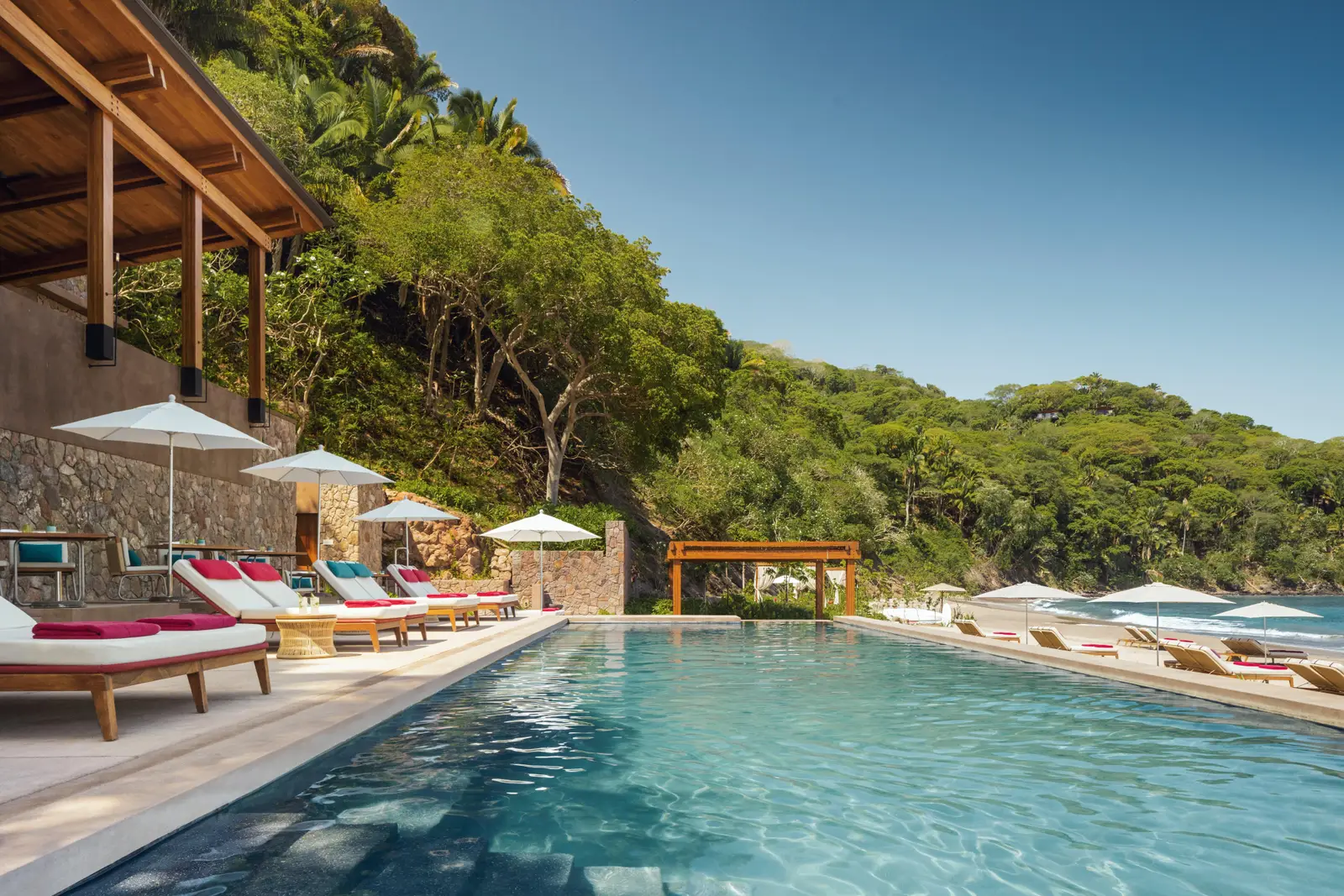 The Jetty Beach Club pool with white parasols, beach and cliff