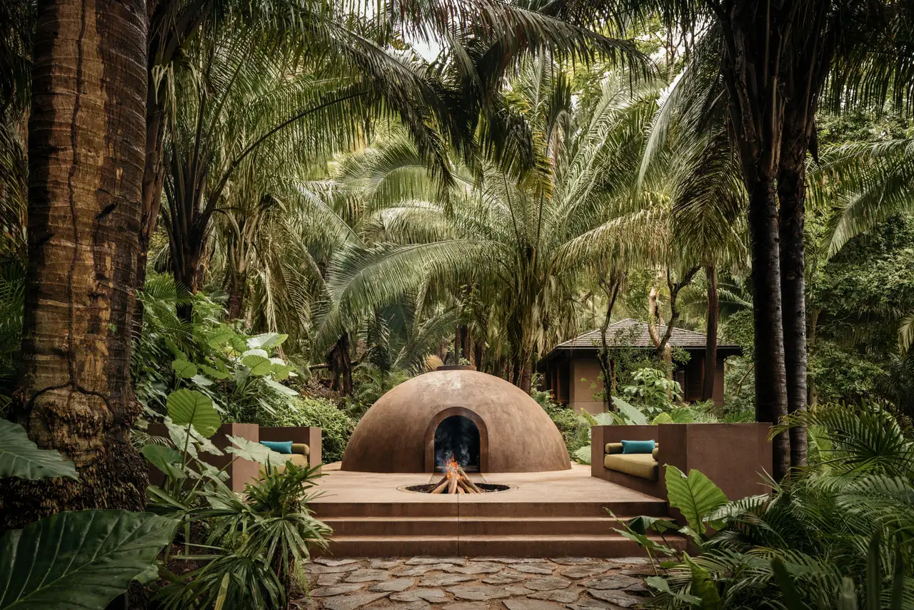 The domed Temazcal with a fire at its entrance and surrounding forest