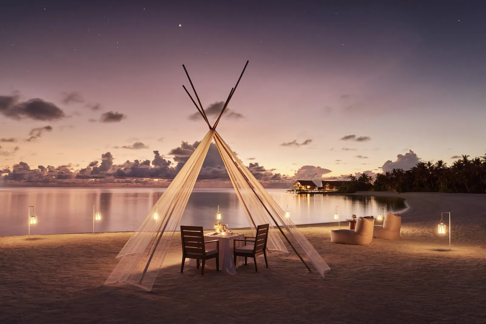 A private dinner on the beach under a wooden canopy, candles lit