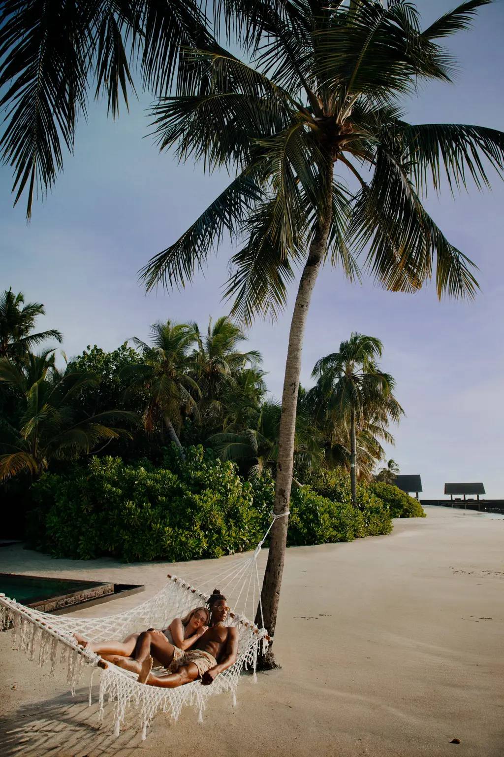 A couple in a hammock strung between 2 palms on the beach