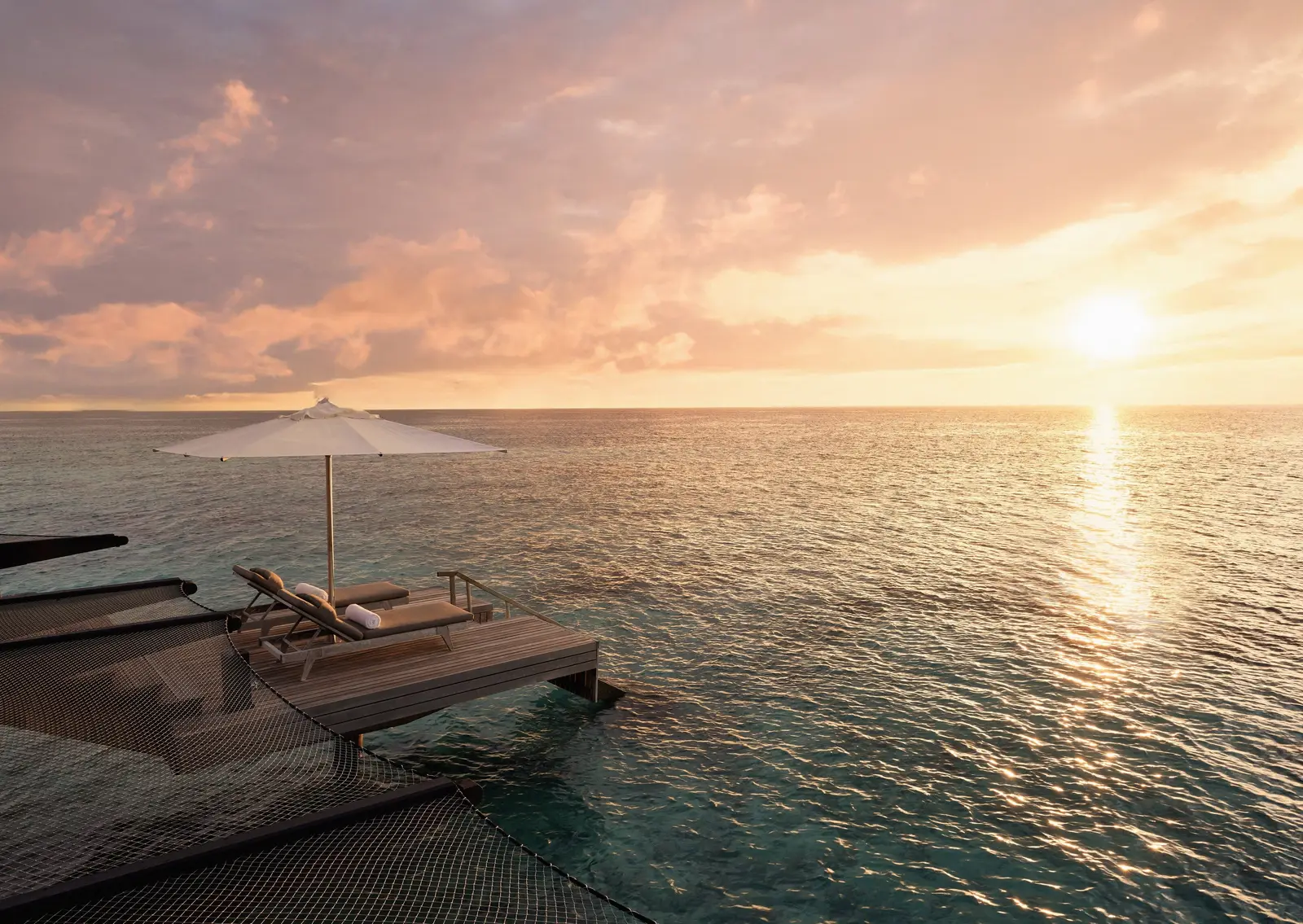 A Water Villa’s deck at sunset, loungers and parasol