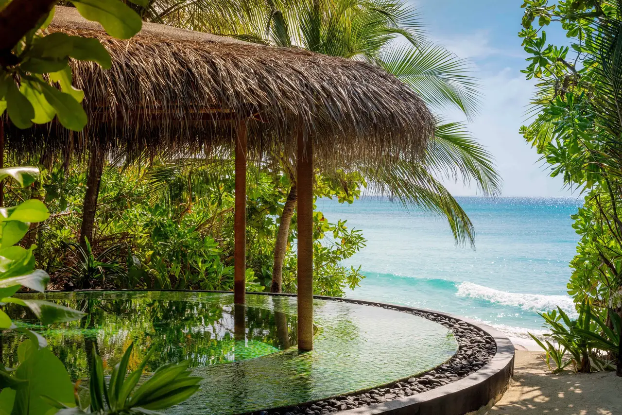 A pavilion by the sea with a round pool, among the palms