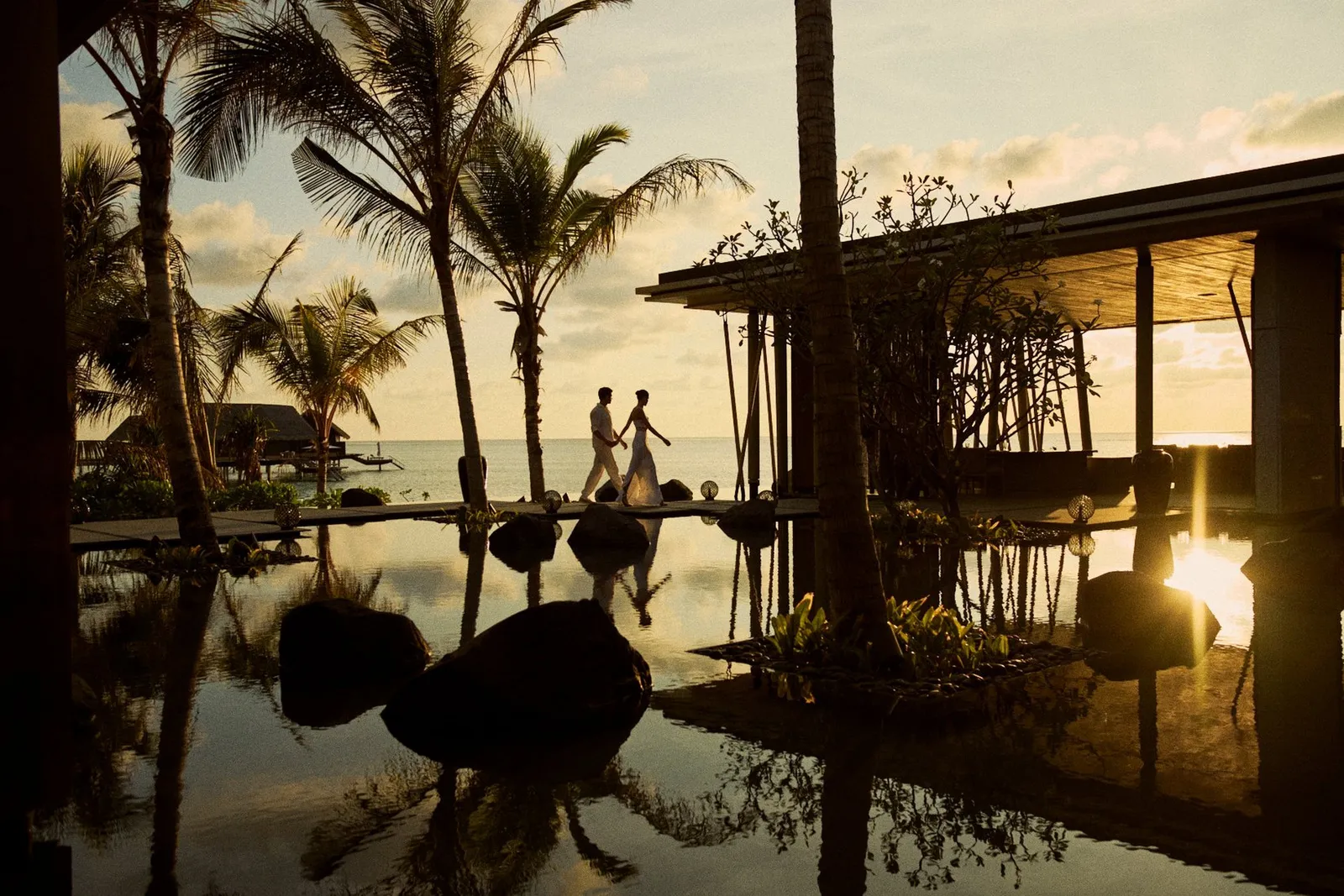 2 guests walking beside TAPASAKE’s lit pool at dusk