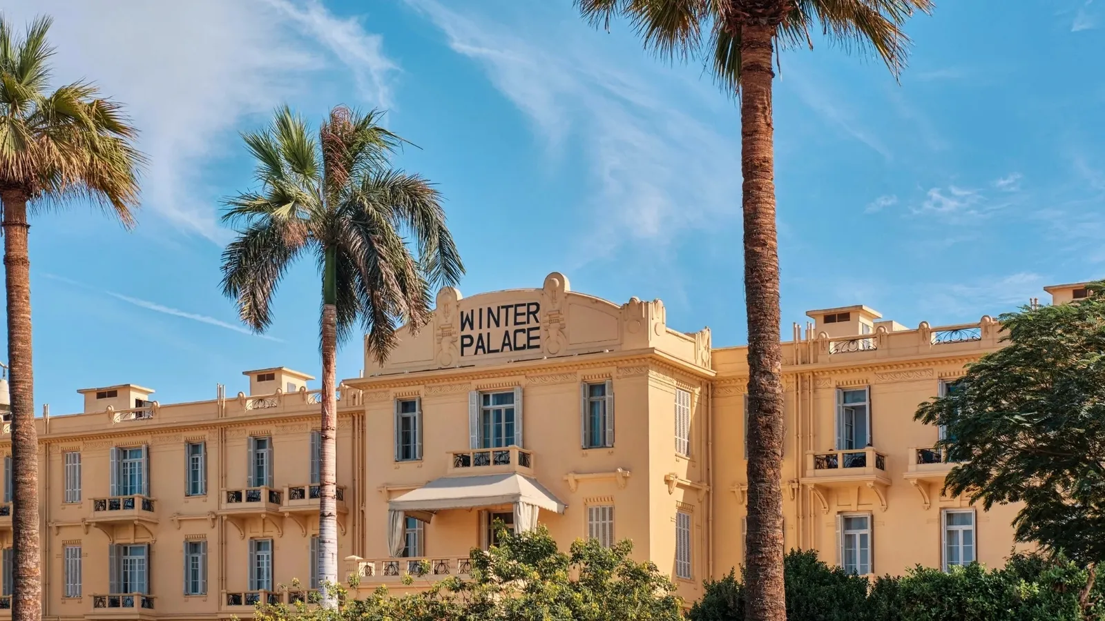 The yellow façade of the Winter Palace in Luxor among the palms