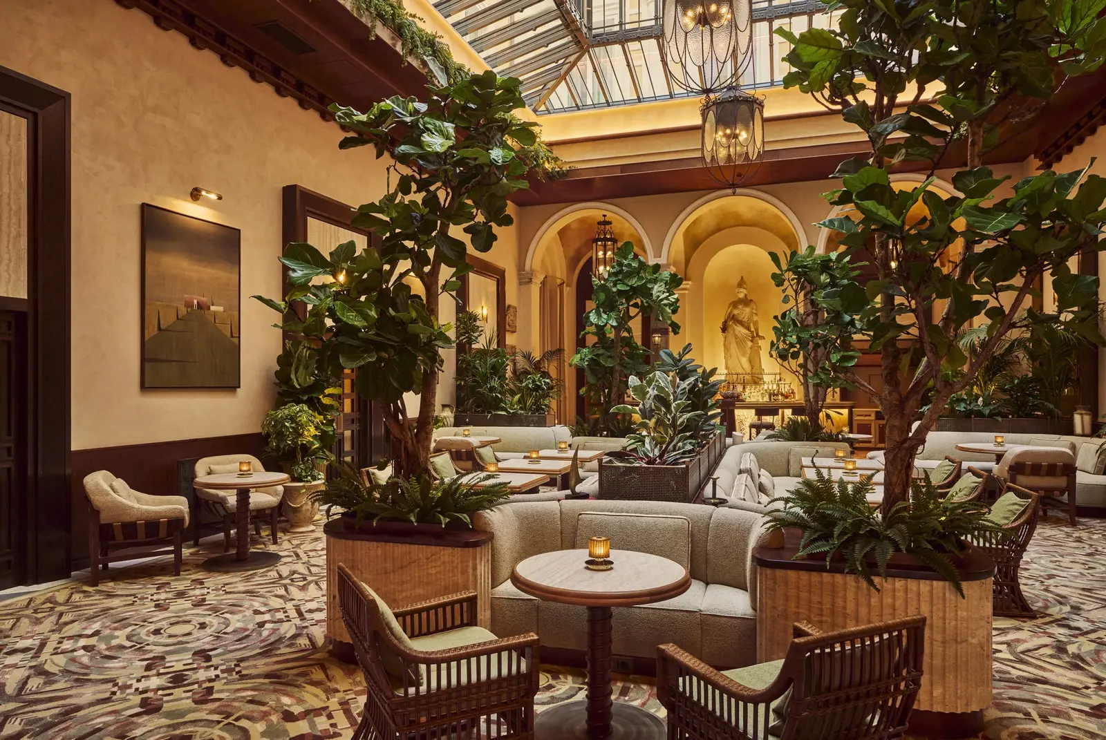 La Minerva Bar in the atrium, among olive trees and armchairs, under the glass-and-iron roof