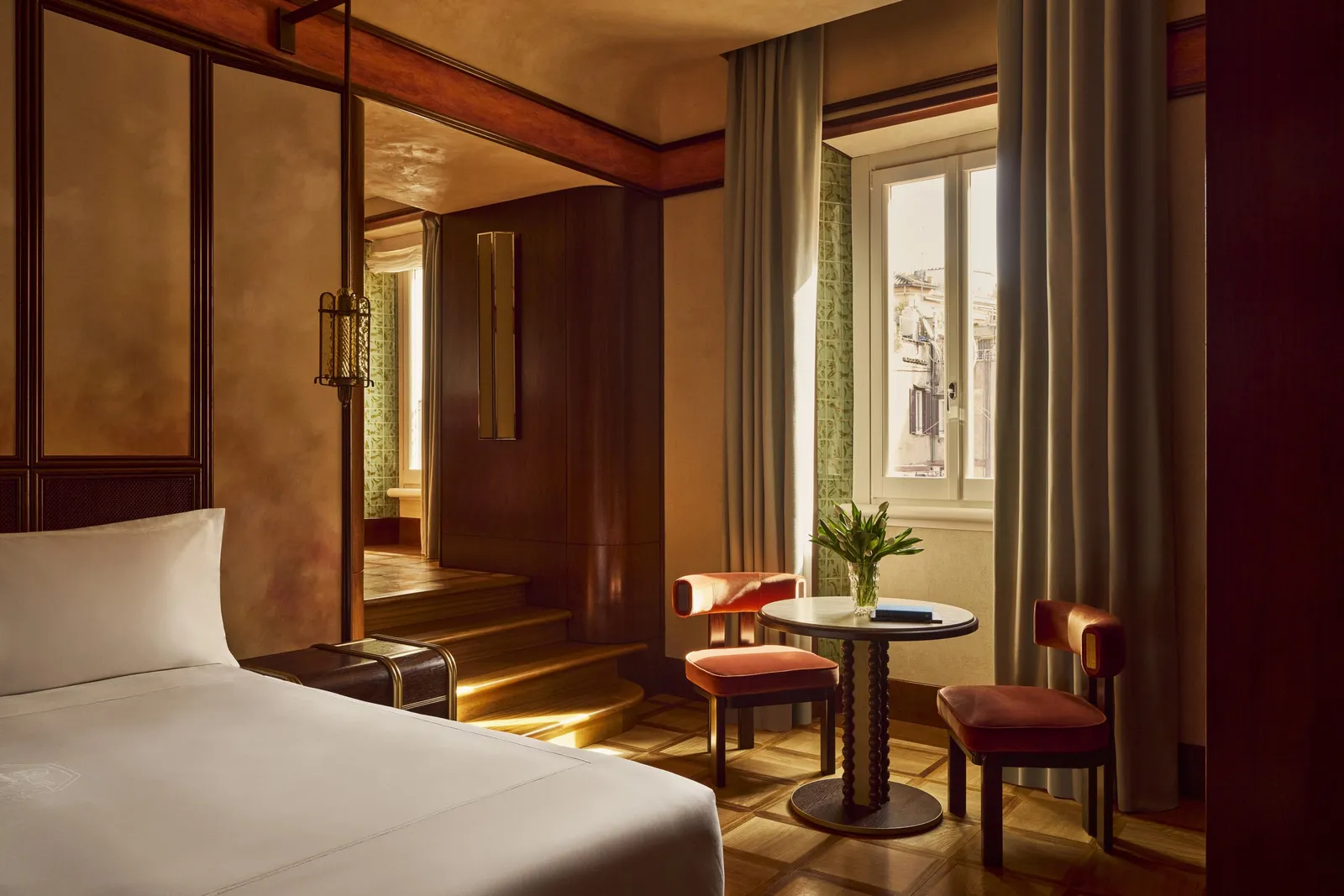 A Deluxe Room with the bed, a table for 2 and a window with a pale curtain