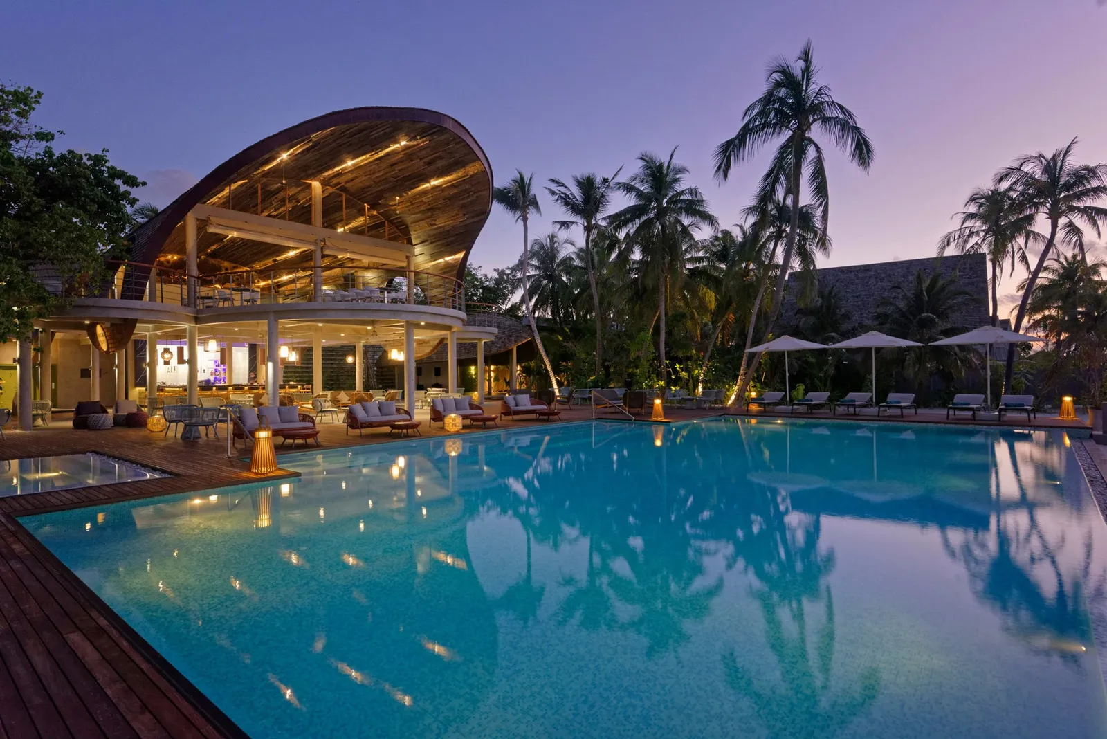 The main pool at dusk, with the Edgewater Bar lit up under its great curved roof and the palms behind.