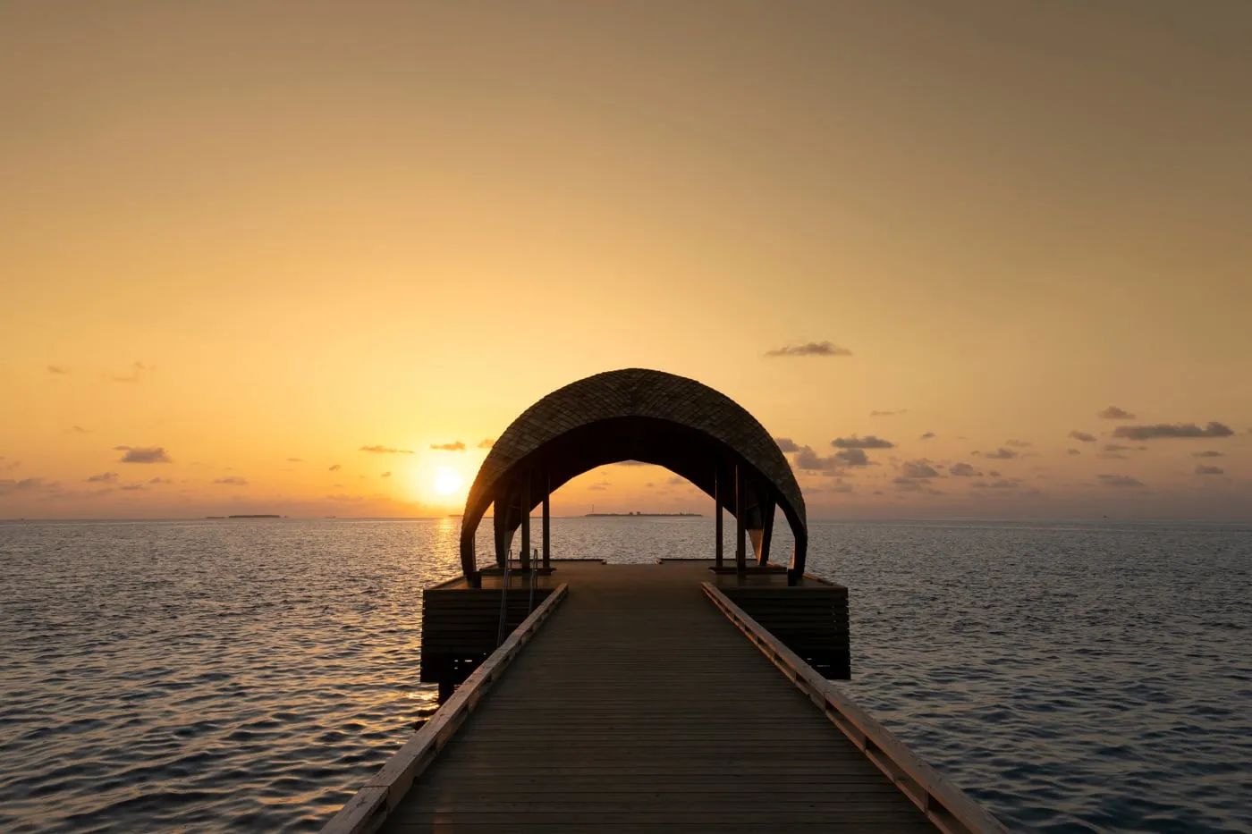 The jetty running out to sea to an arched pavilion, against the light, with the sun low on the horizon.