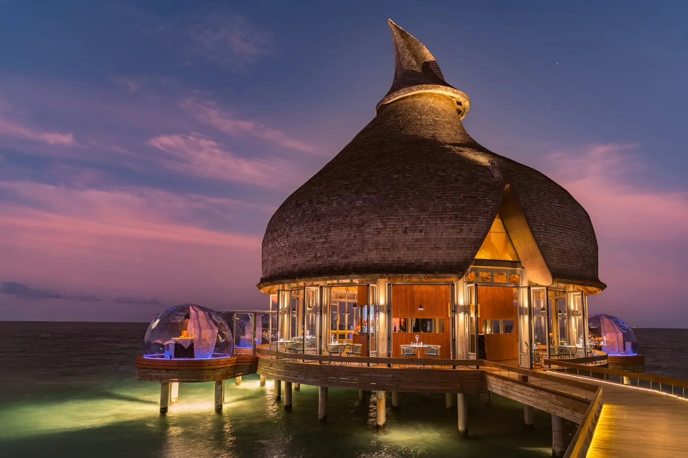 Moodhu Grill in the evening under its pointed thatch, with 2 clear domes for dining over the water.