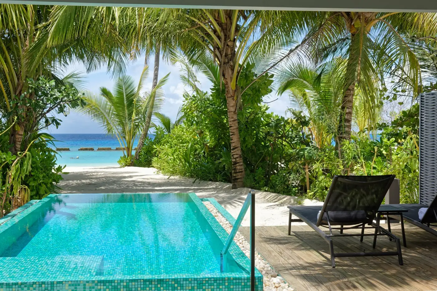 The private pool of a Beach Villa with Private Pool, loungers under the roof and, beyond the palms, the beach and the sea.
