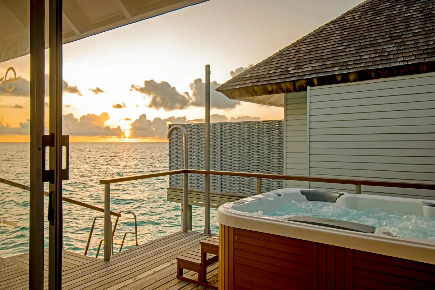 The deck of a Sunset Over Water Villa at sunset, with its hot tub and the ladder down to the sea.